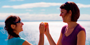 Deux amies se félicitent en se tapant dans la main, en arrière-plan, une mer d’où reflètent les rayons du soleil.