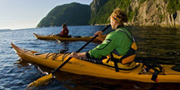 Kayakers paddling by a steep cliff over the Saguenay River.