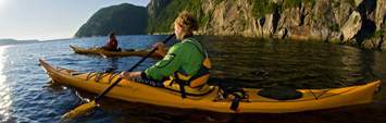 Kayakers paddling by a steep cliff over the Saguenay River.