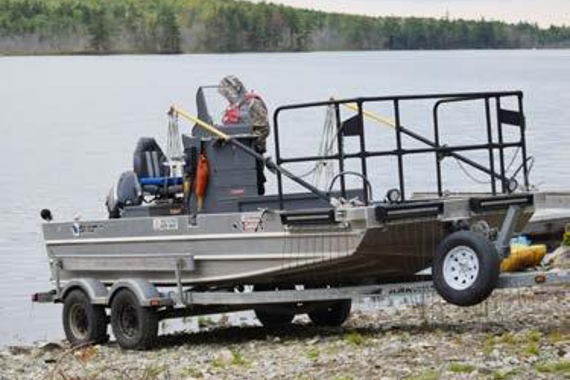A small aluminum boat on a trailer at shoreline.
