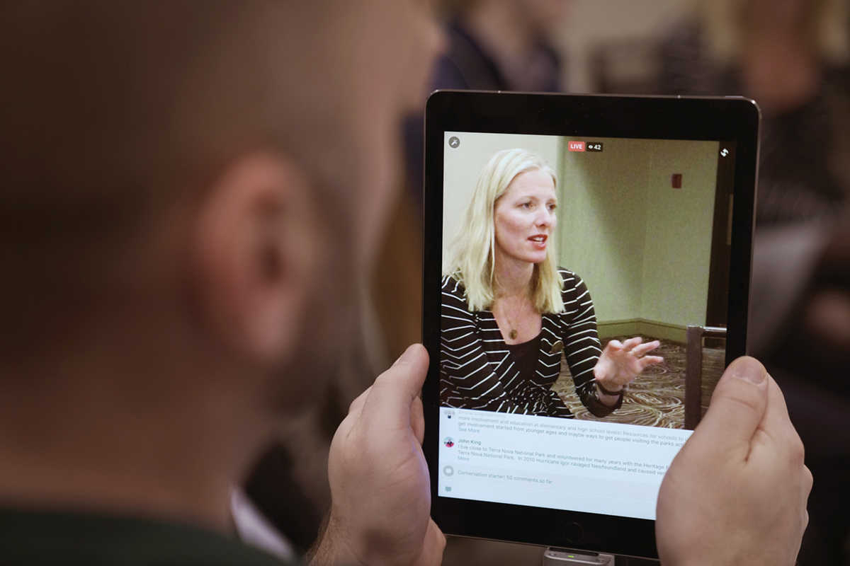 Un homme regarde une vidéo de la ministre McKenna diffusée en direct, sur une tablette électronique pendant une des séances de consultation de Parlons de parcs Canada.