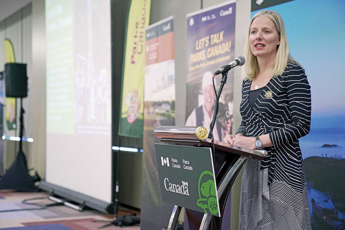 La ministre McKenna debout au podium pendant une des séances de consultation de Parlons de parcs Canada.