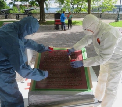 Two persons refurbishing a bronze commemorative plaque