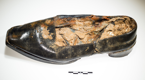 A man’s black low heeled shoe with mud.