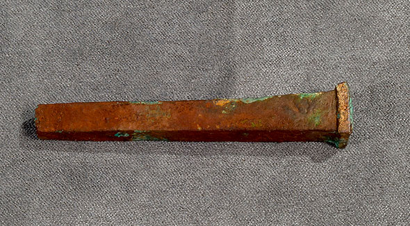 A long rusty rectangle of metal with nail head.