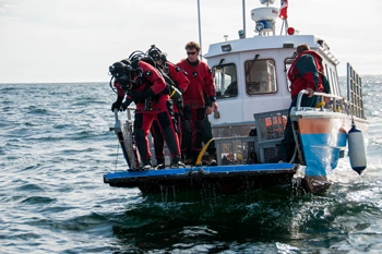 Les plongeurs vêtus en rouge debout sur la poupe du bateau, prêts à sauter dans les eaux turbulentes.