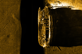 Image of ship’s hull on a darker background. Decking is mostly missing, revealing beams and lower deck.