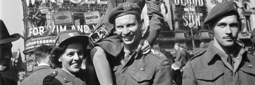 Deux jeunes femmes et un jeune homme souriant et levant un chapeau en l’air.