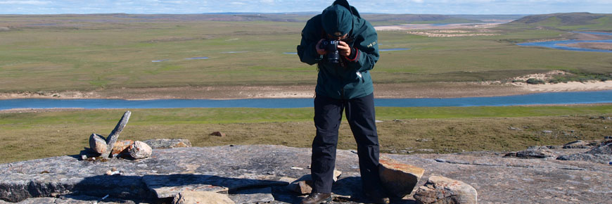 A person in a Parks Canada jacket photographing a stone cache.