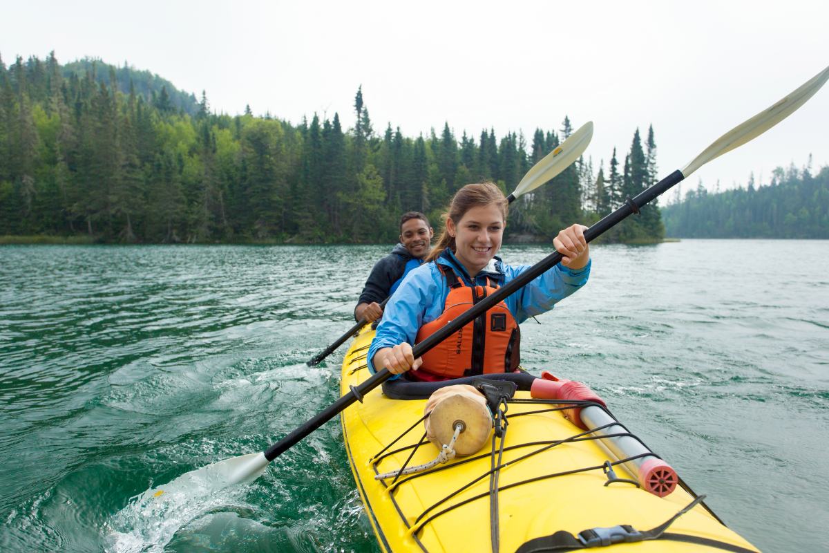 Deux personnes ensemble dans un kayak alors qu’elles pagaient sur une eau bleue verte avec des forêts en arrière-plan.