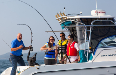 Quatre personnes à bord d’un bateau de pêche affrété sourient à la caméra. L’un tient une canne à pêche tandis que l’autre tient un poisson.