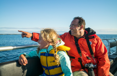 À bord d’un bateau, un père montre l’eau du doigt tandis que sa fille à côté de lui regarde avec enthousiasme dans cette direction.