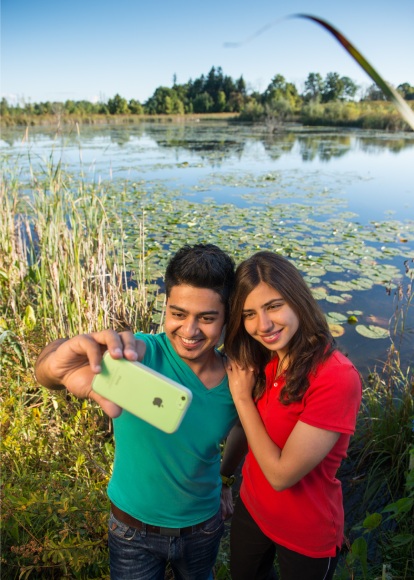 Two smiling young people stand closely together while taking a selfie in front of a wetland.