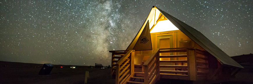 Petite hutte dotée d’un éclairage minimal sous un ciel étoilé.