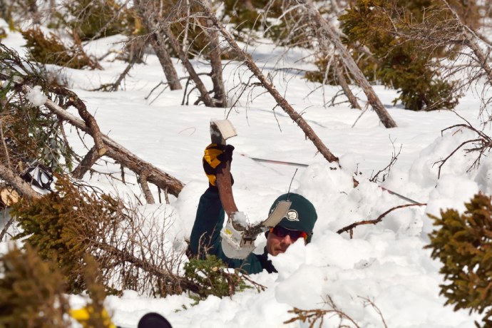 Un employé de Parcs Canada a de la neige jusqu’au cou alors qu’il tient un collier émetteur brisé dans les airs avec sa main gantée.