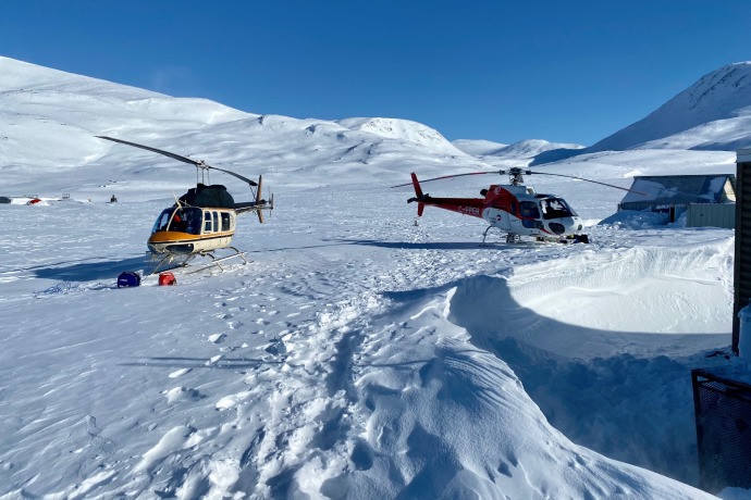 Two helicopters carrying goods and supplies land at a wintry, remote base camp.