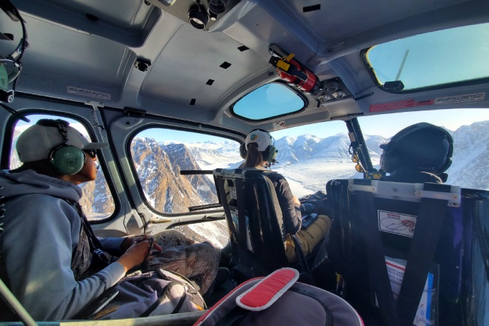 Un passager dans un hélicoptère observe le paysage montagneux couvert de neige en contrebas.