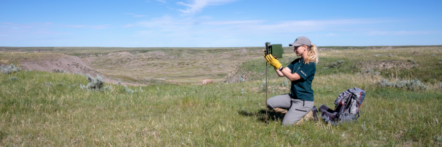 Femme à côté d'une caméra avec un paysage de prairie derrière.