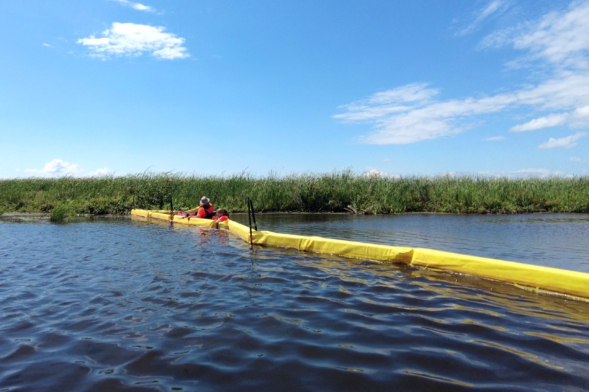 Un membre du personnel de Parcs Canada patauge dans l’eau jusqu’à la poitrine pour installer un barrage à sédiments jaune dans l’eau.