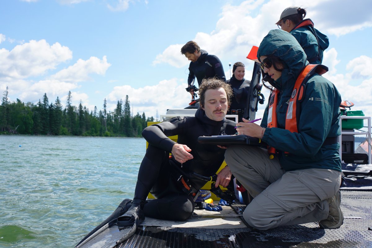 Un plongeur s’entretient avec un membre du personnel de Parcs Canada au sujet de l’un des nids à bord d’une plateforme de plongée, tandis que trois autres personnes travaillent en arrière-plan.