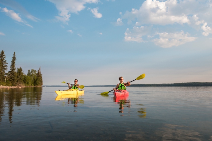 Two boaters use a yellow and a red kayak to paddle through a calm lake.