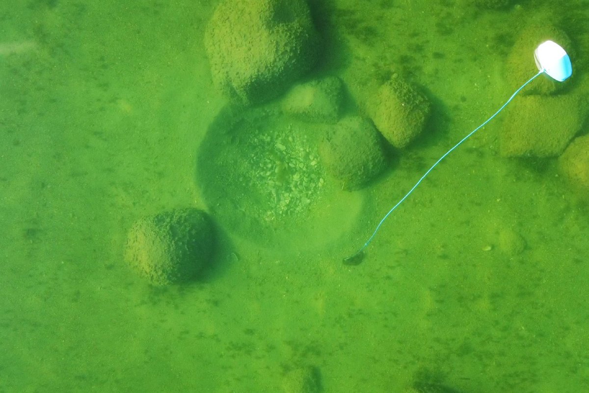 An aerial image of an underwater round divot on the lakebed with a floating buoy beside it.