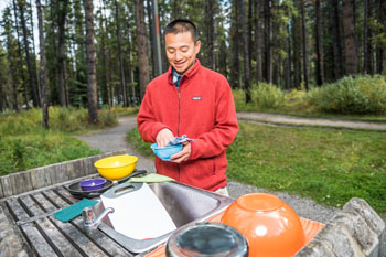 A man washes dishes outdoors.