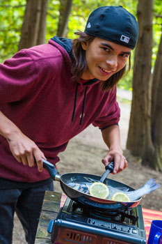 Un jeune cuit un poisson en plein air.