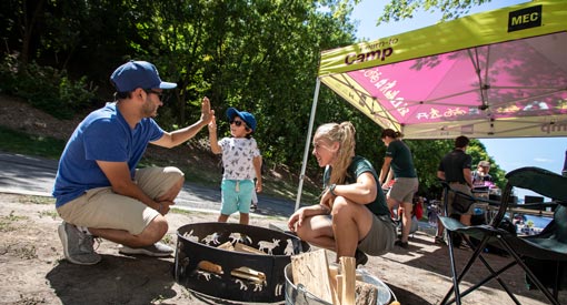Father and son learning how to make a campfire with a uniformed Parks Canada staff (Emma Lindale) at a Learn-to Camp pop-up booth along the Rideau Canal.