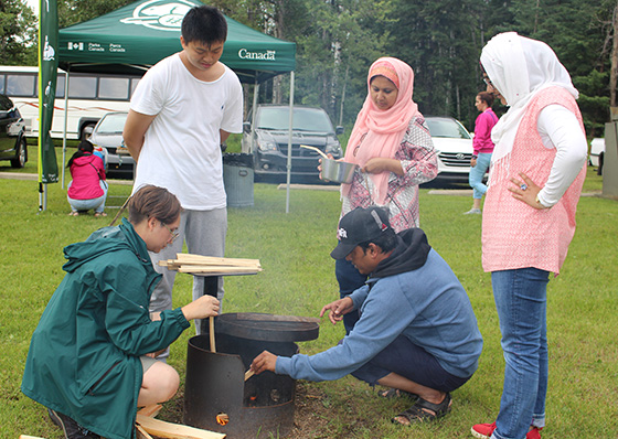 A Parks Canada employee helping four new Canadians build a fire at a Prince Albert National Park Learn-to Camp event.