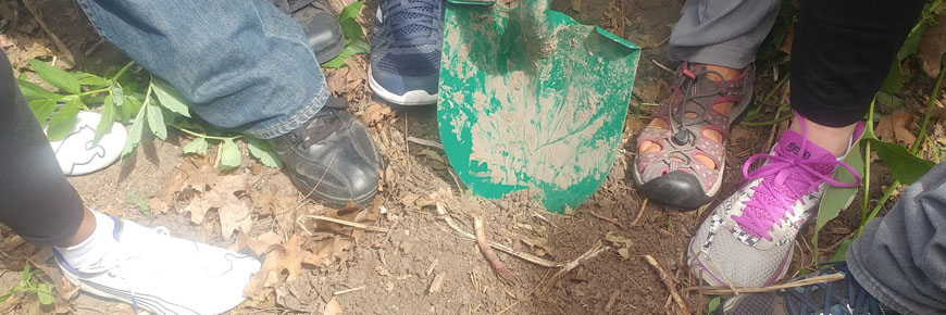 Photo of hikers’ feet with shovels beside them.