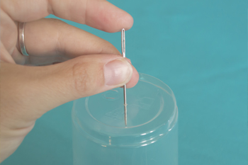 An adult hand pierces the bottom of the cup with a needle