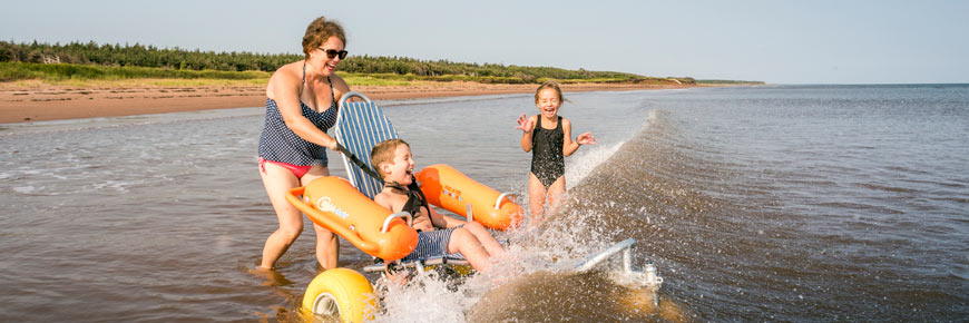 A family with accessibility needs enjoys a swim in the ocean with a beach wheelchair at Stanhope Beach. 