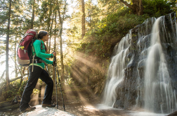  A female hiker marvels at the picturesque waterfall at Bonilla Creek, on the West Coast Trail, as the sun’s rays shine through the trees. 