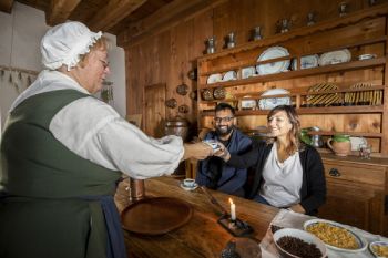 Deux adultes et un guide dégustent du chocolat chaud à la forteresse de Louisbourg.