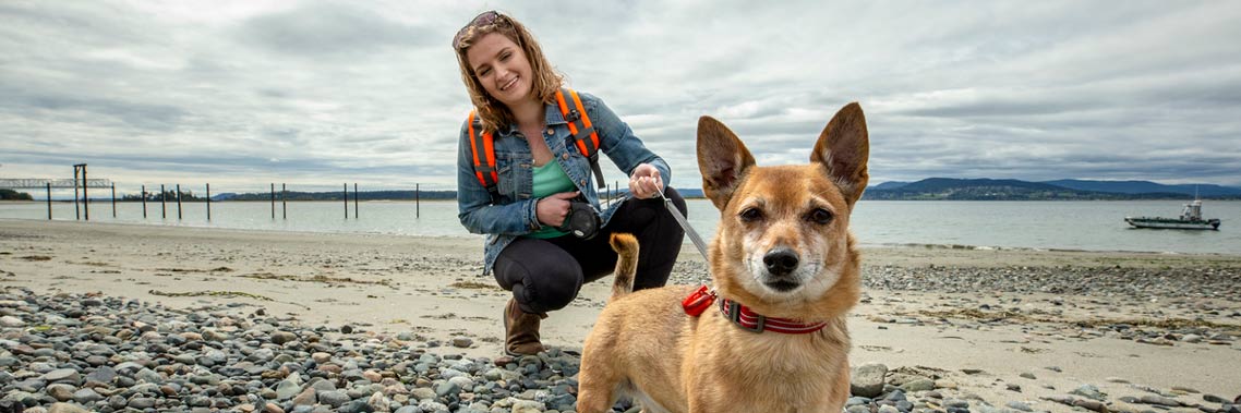 A young woman walks with her dog on leash at Sidney Spit. 