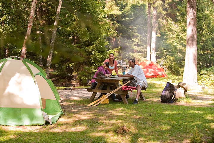 Trois personnes prennent leur repas à la table de pique-nique de leur site de camping par une journée ensoleillée.