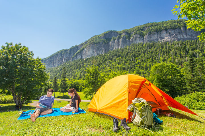 Deux jeunes adultes font de la lecture devant leur tente au terrain de camping Cap-Bon-Ami.