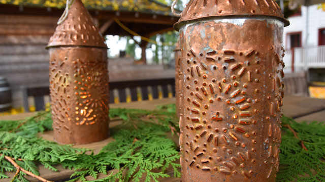 Two lit copper lanterns standing on an outside table.