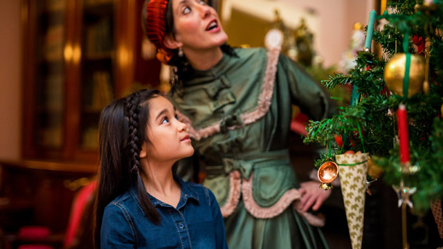 Une jeune fille, en compagnie d’une guide portant une robe de l’époque victorienne, est émerveillée en regardant les décorations d’époque dans un sapin.