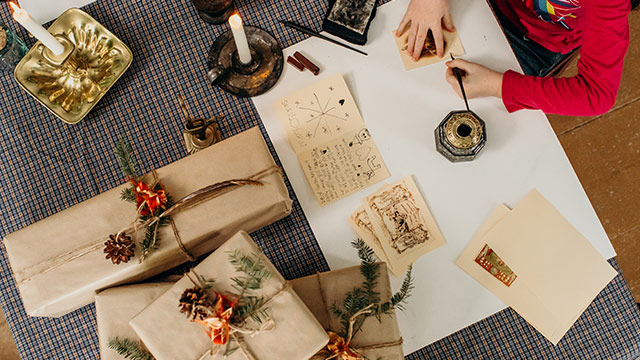 A child practicing writing with a quill ink pen surrounded by traditionally wrapped gifts.