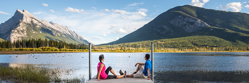 A couple enjoys evening views of the mountains from a dock at Vermillion Lakes in Banff National Park. 