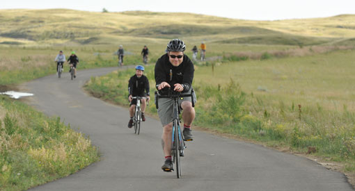 Des cyclistes roulent sur la promenade des Badlands avec des collines verdoyantes en arrière-plan.