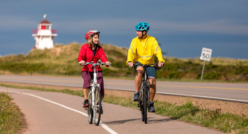 Deux cyclistes à vélo sur le sentier du Golfe avec le phare de Covehead en arrière-plan.