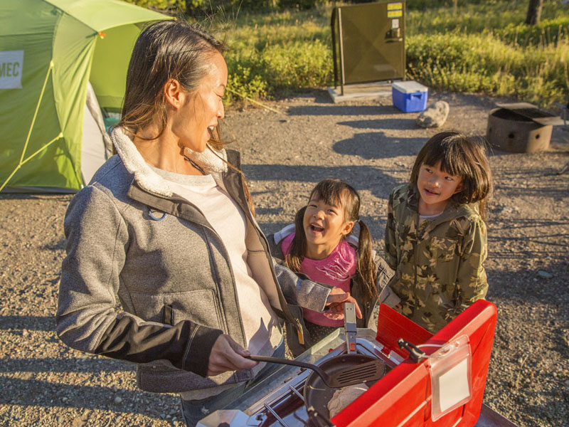 Une maman et ses deux filles sur un emplacement de camping équipé.