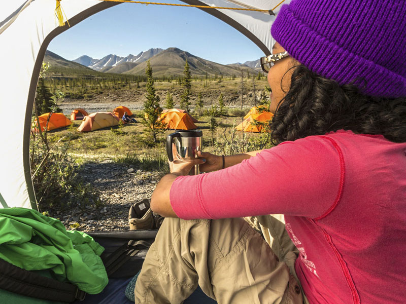 Une femme assise dans sa tente, regarde à l'extérieur en direction d'un groupe de tentes à proximité.