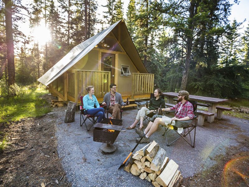A group of young adults around a campfire beside an oTENTIK at Whistlers Campground, in Jasper National Park.