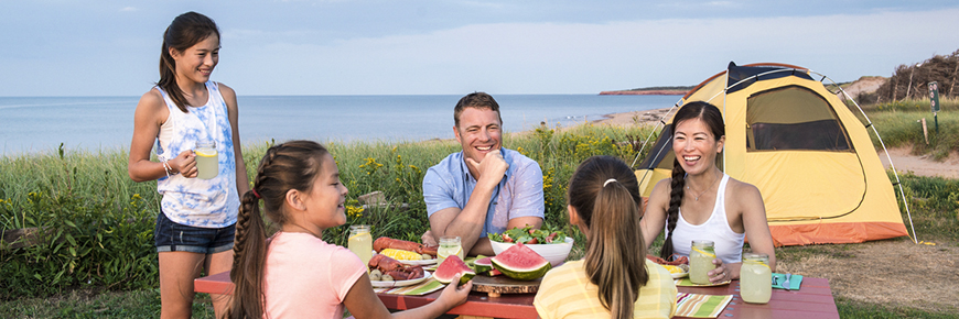 A family enjoys dinner at the picnic table of their waterside campground.