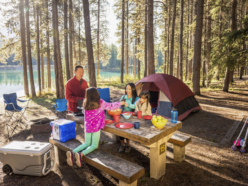Une famille déjeune à la table de pique-nique de leur emplacement de camping en bordure de l'eau lors d'une matinée automnale.