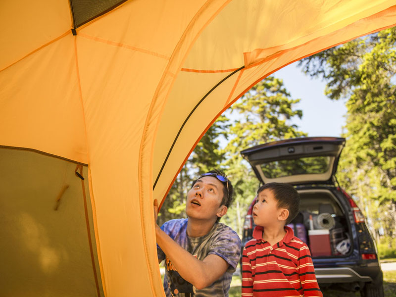A young boy helps his father set up a tent.